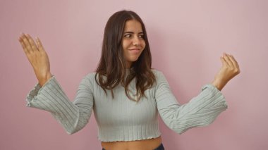 Pembe arka planda şakacı hareketler yapan bir kadın, kendine güvenini ve neşesini sergiliyor, esmer saçları yüzünü güzelce çerçeveliyor..