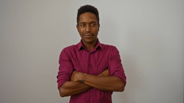 Kolları çapraz duran genç adam beyaz arka planda kendine güvenini ve tarzını ifade ediyor.