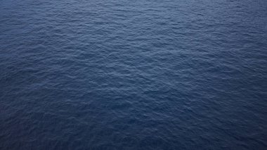 Dalgalanan mavi suyun olduğu sakin okyanus manzarası berrak bir gökyüzünü yansıtıyor, dinginlik ve yaz tatilini çağrıştırıyor..