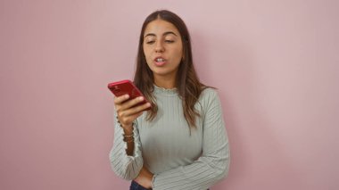Akıllı telefonuyla sesli mesaj gönderen bir kadın, izole edilmiş pembe bir arka plana karşı duruyor, modern iletişimi gündelik bir ortamda temsil ediyor..