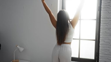 Parlak oturma odasında uzanan ve büyük bir pencereden içeri güneş ışığı süzülen bir kadın modern apartman ortamında sakin ve sakin bir atmosfer yaratıyor..