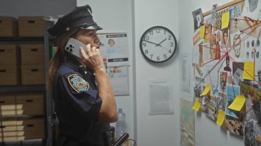 Odaklanmış bir kadın polis memuru, telefonda kanıt, harita ve notlarla çevrili bir ofiste araştırma yapar..