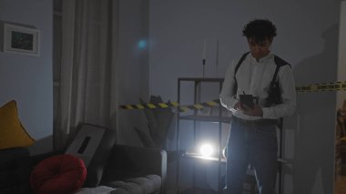 Pantolon askılı İspanyol adam, kapalı bir suç mahallinde dikkat bandıyla notlar alıyor..