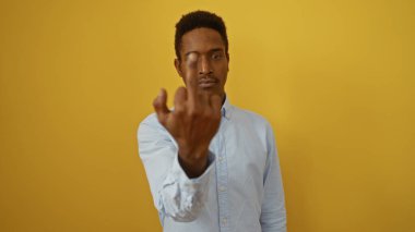 Genç bir adam, canlı sarı bir arkaplan karşısında dikilirken davranışlarını ve duygularını izole bir ortamda ifade ederken bir jest yapıyor..
