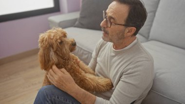 Latin kökenli olgun bir adam sıcak bir oturma odasında kaniş tutuyor..