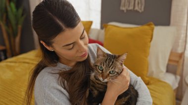 Genç bir İspanyol kadın sıcak bir yatak odasında yatağında evcil kedi yavrusunu tutuyor..