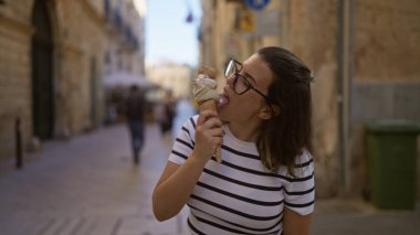Genç bir İspanyol kadın güneşli bir günde Puglia, İtalya 'nın büyüleyici caddelerinde yürürken dondurma külahını yalamaktan zevk alır..