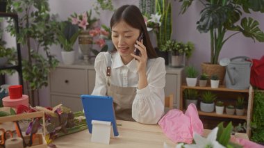 Bir çiçekçide tablet kullanan ve telefonla konuşan Asyalı kadın..