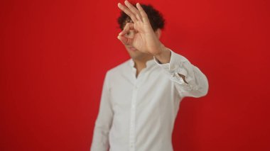 Beyaz tişörtlü genç bir İspanyol, izole edilmiş kırmızı arka planda iyi bir jest yapıyor.
