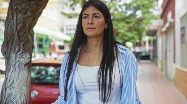 Şehir caddesinde uzun esmer saçlı güzel bir kadın, çizgili bir gömlek giyiyor, kalabalık bir şehir bölgesinde açık havada..