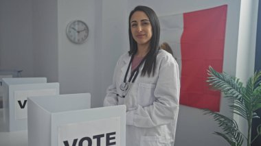 Steteskoplu, laboratuvar önlüklü kendine güvenen bir kadın oy kabininde Meksika bayrağının önünde duruyor..