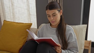 Güzel, genç bir İspanyol kadın, evdeki rahat bir yatak odasında yatağında oturmuş kitap okuyor..