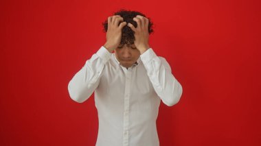 Beyaz gömlekli stresli bir İspanyol, kırmızı arka planda başını tutuyor.
