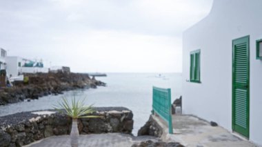 Beyaz binalar, yeşil kepenkler ve bulutlu bir gökyüzünün altında deniz boyunca uzanan kayalık kıyı şeridi.