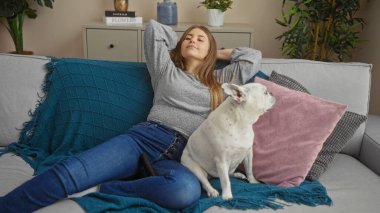 Kafkasyalı genç bir kadın evcil köpeğiyle oturma odasındaki kanepede dinleniyor..