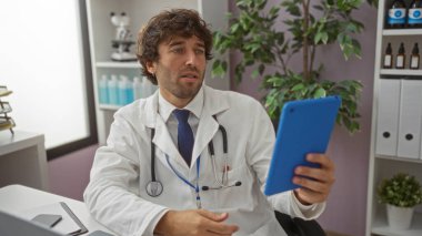 Yakışıklı İspanyol erkek doktor klinikte tablet kullanıyor, profesyonellik gösteriyor ve ev bitkileri ve tıbbi ekipmanlarla modern bir sağlık ortamında odaklanıyor..