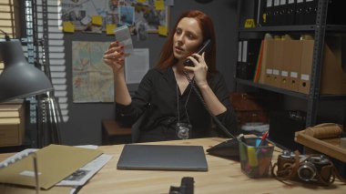 Genç bir kadın, soruşturma dosyalarıyla çevrili bir dedektifin ofisinde telefonla konuşurken kanıtları inceliyor..