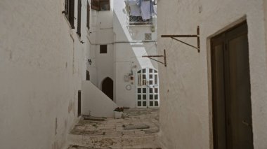 Ottuni, puglia, İtalya 'da beyaz yıkanmış binaların bulunduğu pitoresk dar bir ara sokakta güneşli bir cadde, çamaşırhane ve otantik İtalyan mimarisi yer alıyor..