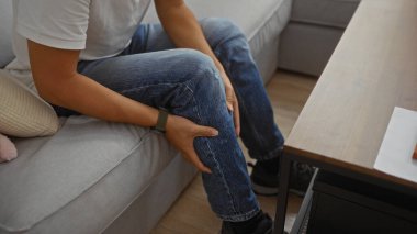 Oturma odasında bacağını tutarak oturan genç adam.