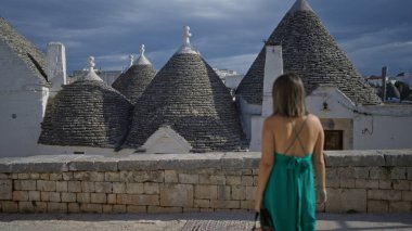 Genç bir İspanyol kadın, eski Alberobello, Puglia, İtalya 'nın büyüleyici bir Avrupa caddesinde ikonik trulli çatılarını gözlemliyor..