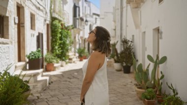 Genç, güzel bir İspanyol kadın, tarihi locorotondo, puglia, İtalya 'nın büyüleyici beyaz sokaklarını keşfediyor. Etrafı yemyeşil bitkiler ve sıcak Akdeniz mimarisi ile çevrili..