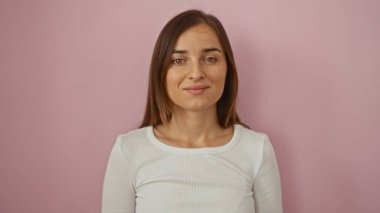 Çekici ve kendine güvenen, pembe bir arka planda duran kahverengi saçlı, güzel, genç bir kadın..