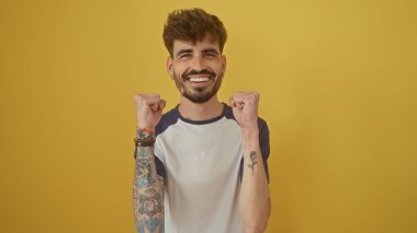 Dövmeleri olan neşeli genç adam, parlak sarı bir arka plana karşı başarısını kutluyor..