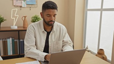 Modern bir ofis düzeninde dizüstü bilgisayarla çalışan sakallı yakışıklı bir genç..