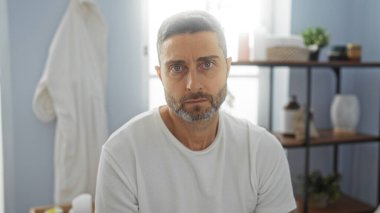 Yakışıklı bir adam sakin bir spa odasında dinleniyor, arka planda hafif ışıklandırma ve sağlık ürünleriyle sakin bir ortam sunuyor, biraz sükunet sunuyor..