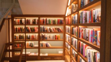 Blurred background of a defocused library setting with bookshelves filled with books under warm lighting clipart