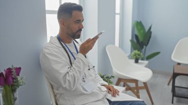 Beyaz önlüklü genç bir İspanyol, kliniğin bekleme odasında akıllı telefon kullanıyor.