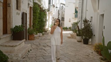 Genç bir İspanyol kadın, Locorotondo, Puglia, İtalya 'nın büyüleyici ve dar sokaklarında dondurma yiyor. Etrafı beyaz binalar ve yemyeşil alanlarla çevrili..
