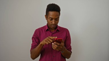 Beyaz arka plan üzerinden izole edilmiş akıllı telefon kullanan genç bir Afrikalı Amerikalı. Modern teknolojiyi ve iletişimi özetleyen yakışıklı yetişkin bir erkeğe odaklanmış minimalist bir ortamda.