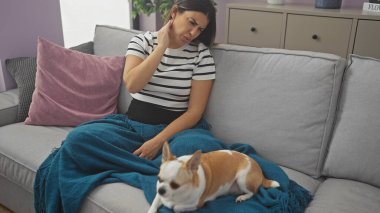 Boyun ağrısı olan genç bir kadın evcil köpeği Chihuahua ile birlikte evin içinde bir kanepede dinleniyor..