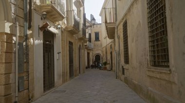 Lecce, Puglia, İtalya 'da dar bir ara sokak tarihi taş binaları olan Avrupa, scooter kullanan bir kişi ve öğleden sonra güneşinin altında gölgeler bırakan balkonlar..