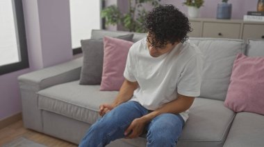 Düşünceli bir İspanyol adam evdeki kanepesinde tek başına oturuyor, rahat bir oturma odasında bir panikleme hissi uyandırıyor..