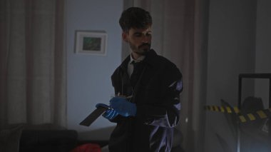 İspanyol bir adam, loş ışıklı bir oturma odasında, eldivenli bir bıçakla bir suç mahallini araştırıyor..