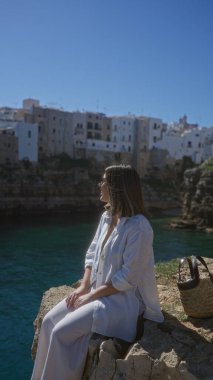 Genç İspanyol kadın polignano 'da kayalık bir uçurum boyunca manzaranın tadını çıkarıyor. Bir kısrak, puglia, İtalya, arka planda deniz ve ikonik beyaz binalar..