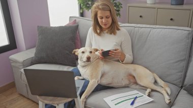 Köpeği rahat bir oturma odasında dinlenirken hesap makinesi kullanan bir kadın.