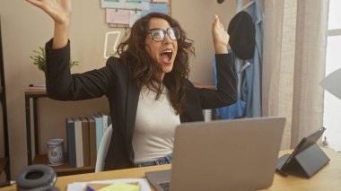Heyecanlı kadın ev ofisinin başarısını kutluyor, dizüstü bilgisayarın önünde kollarını kaldırıyor..
