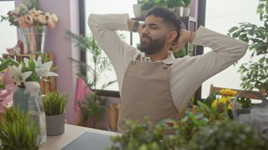 Sakallı genç bir İspanyol, çiçekçi dükkanındaki canlı bitkilerin arasında biraz dinlenir..