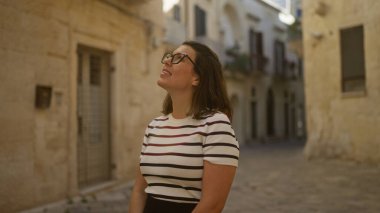 Güzel, genç, İspanyol bir kadın güneşli bir günde tarihi bir mimariyle çevrili büyüleyici, dar bir sokakta gülümsüyor..