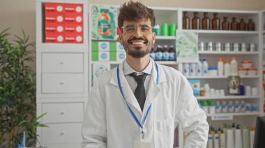 Yakışıklı İspanyol eczacı eczanede beyaz önlüklü gülümsüyor.