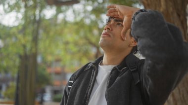 Genç, yakışıklı İspanyol bir adam şehir parkında yukarı bakarken gözlerini koruyor..