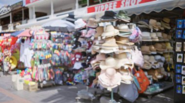 Açık hava pazarında renkli şapka ve aksesuarların odaklanmamış görüntüsü parlak güneş ışığı altında çeşitli ürünler sergiliyor.