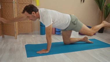 Olgun bir adam paspasın üzerinde yoga yapıyor şık bir dekorasyonla, denge ve zindelik gösteriyor..