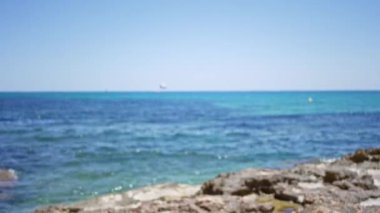 Açık mavi gökyüzünün altında turkuaz deniz ve kayalık kıyı manzarası