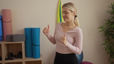 Kadın, yoga minderleri, egzersiz topları ve arka planda yeşillik ile spor salonunda mutlu bir şekilde dans ediyor, neşe ve refahı ifade ediyor..