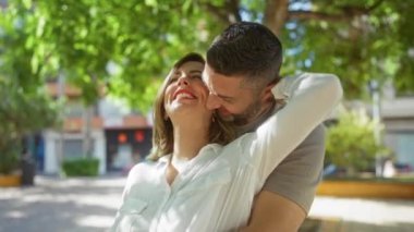 Güneşli bir günde şehir parkında kucaklaşan mutlu çift, birlikte gülüyor ve dışarıda eğleniyorlar..