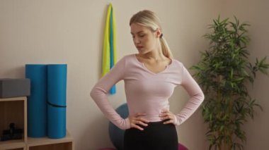 Spor salonundaki kadın antrenmandan sonra terini siliyor. Yoga minderleri ve halterler de dahil olmak üzere spor aletleriyle çevrili..